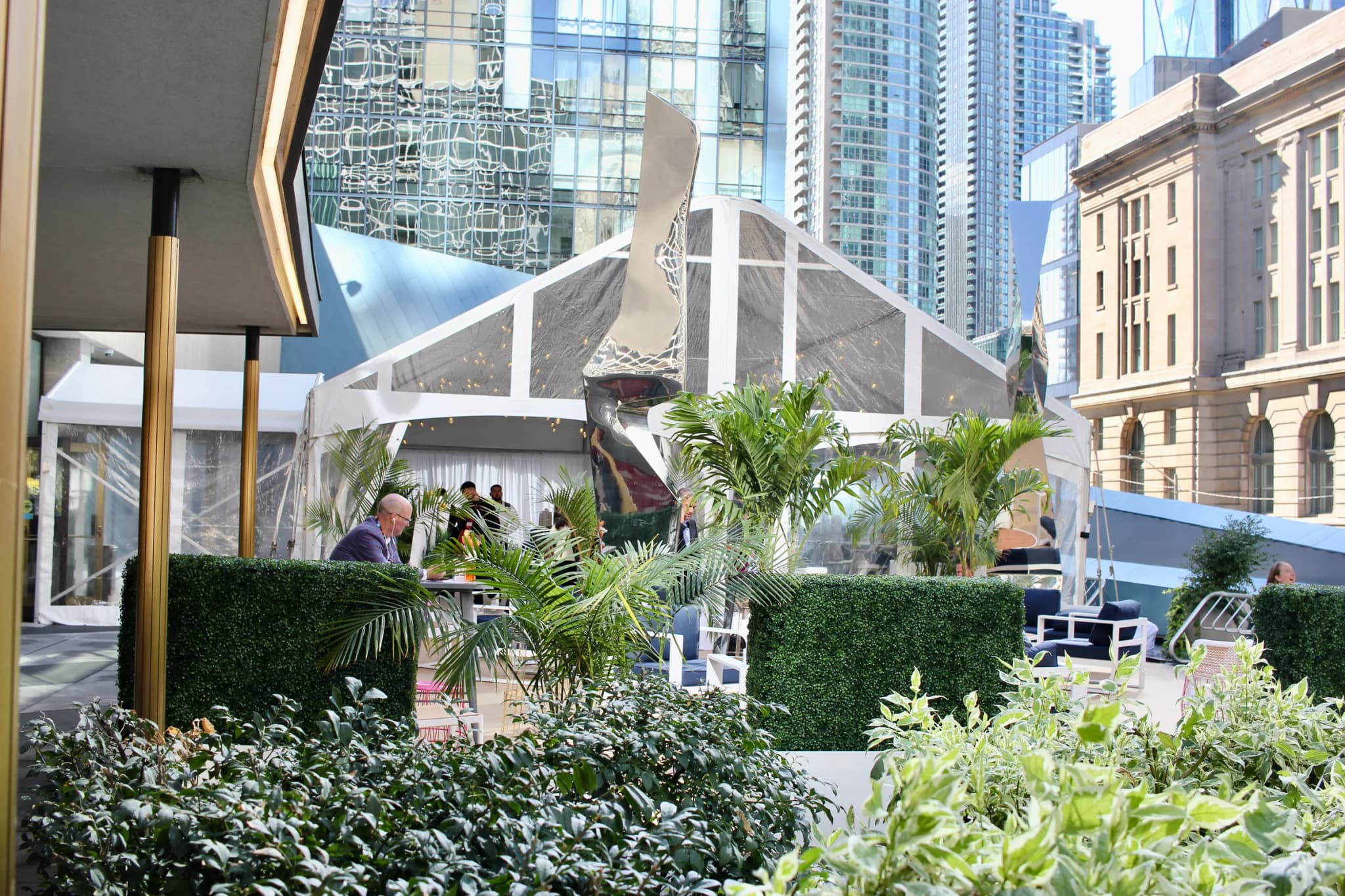 Outdoor event space at Elevate Festival with tropical palms, boxwood hedges and clear tent structure in downtown Toronto