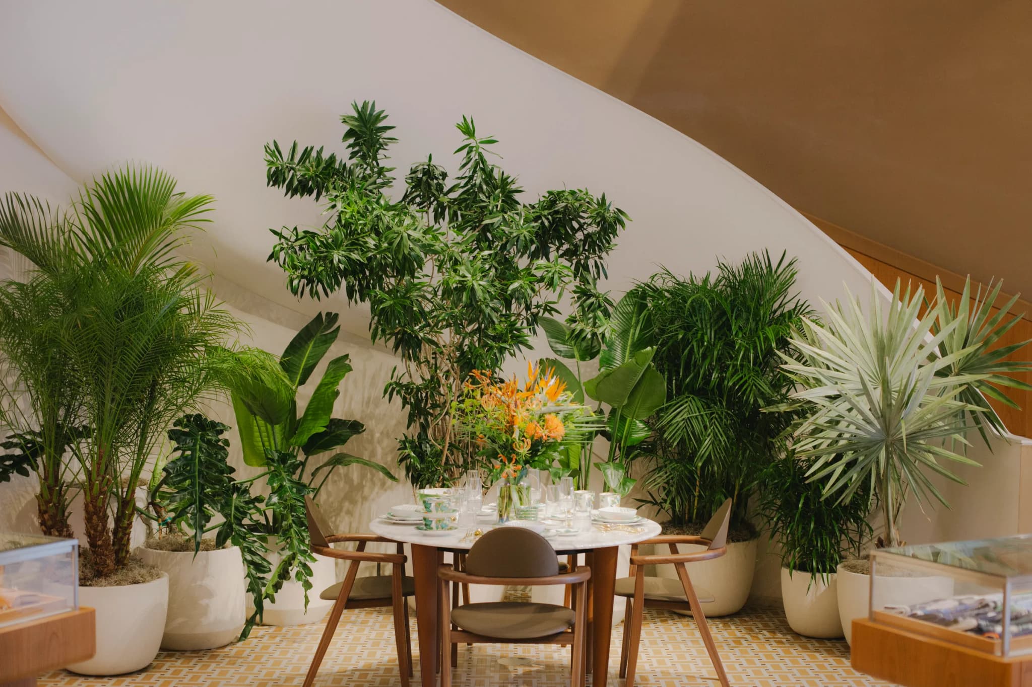 Wide view of tropical plant installation with Areca palms, Bird of Paradise, Monstera and Schefflera surrounding elegant table setting at Hermès Yorkville in Toronto
