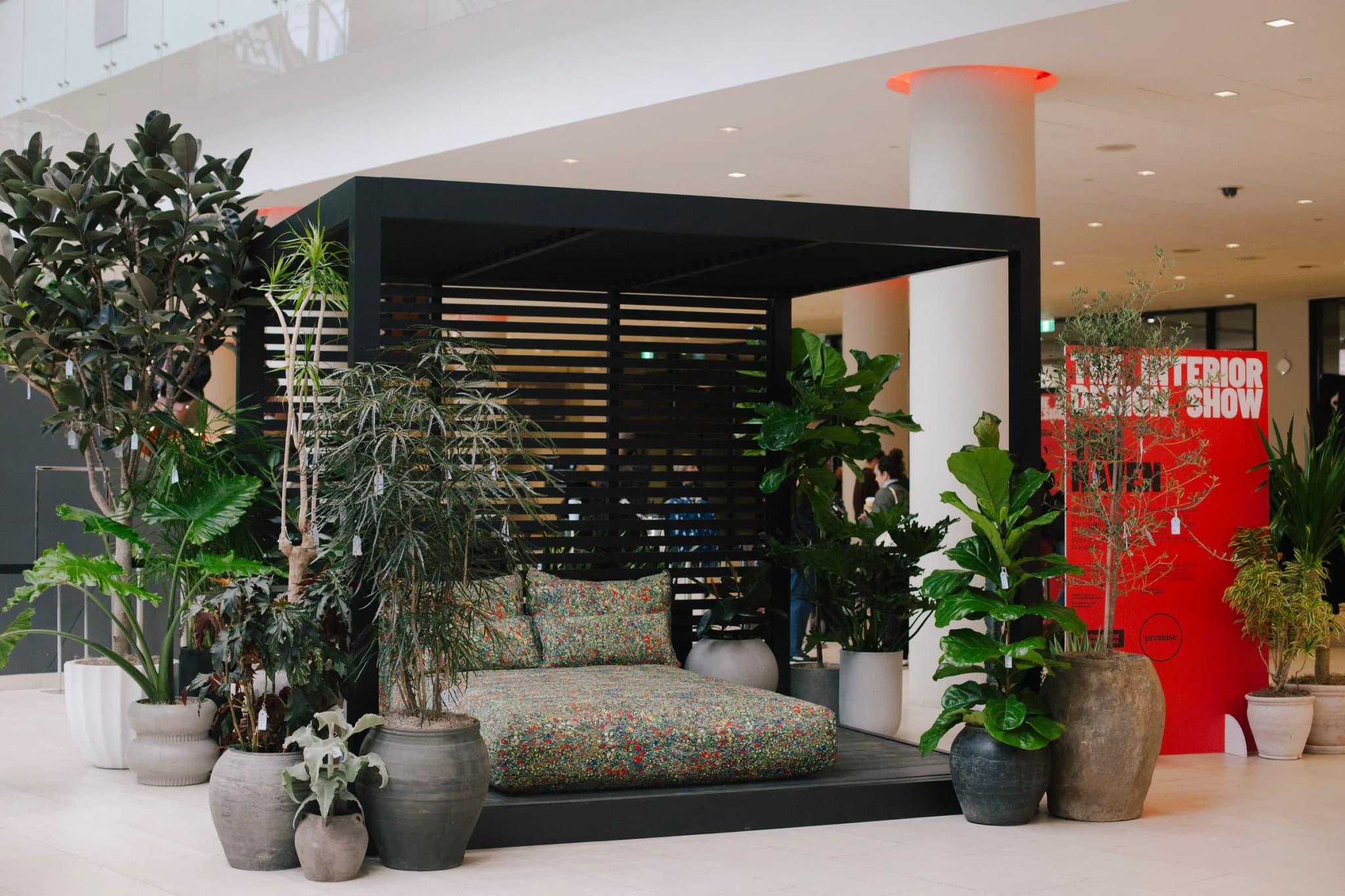 The Haven booth at Interior Design Show featuring wooden pergola structure with hanging greenery and Ficus tree with EV car