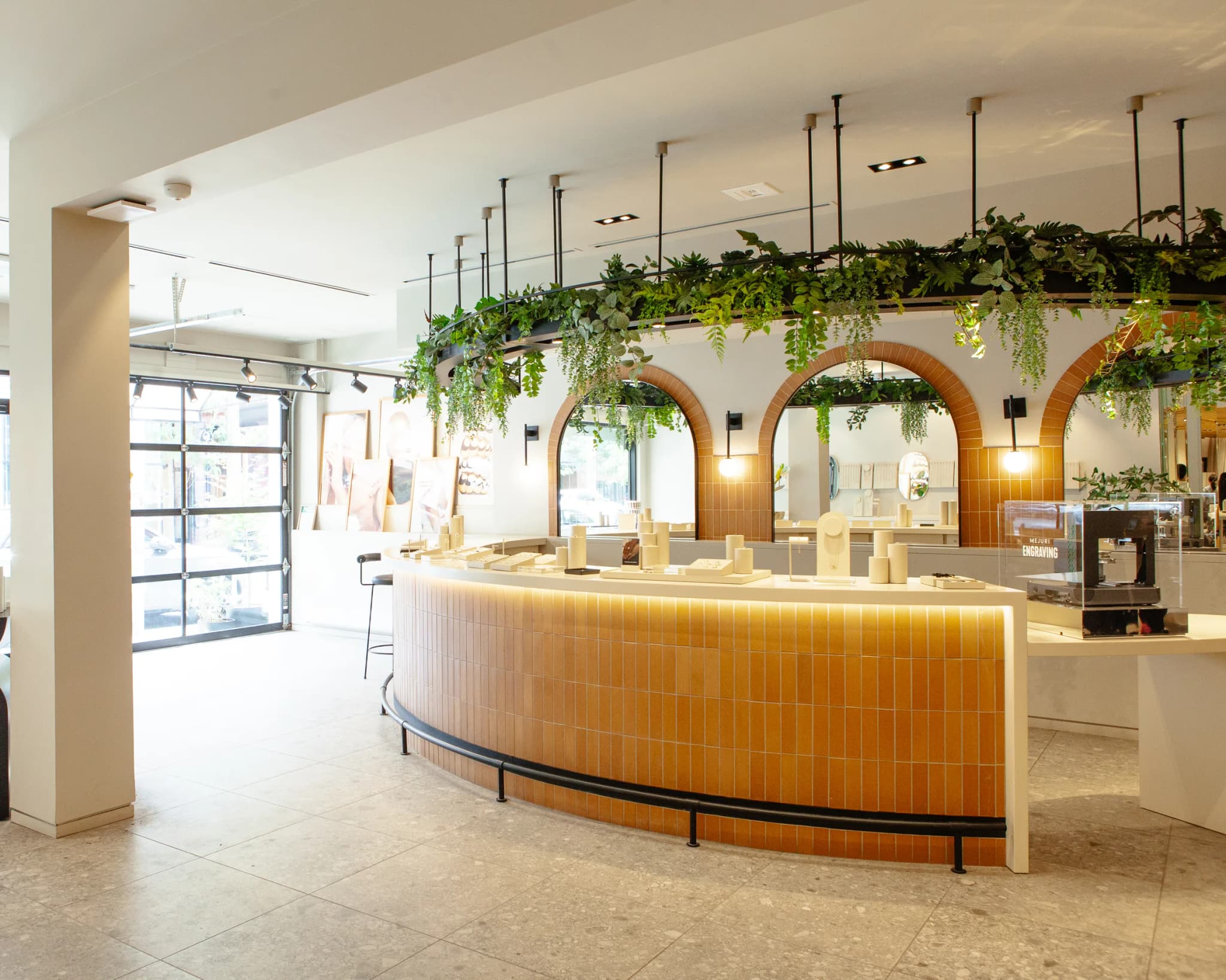 Curved terracotta tile counter with hanging pothos and ferns under arched mirrors at Mejuri Ossington jewelry store