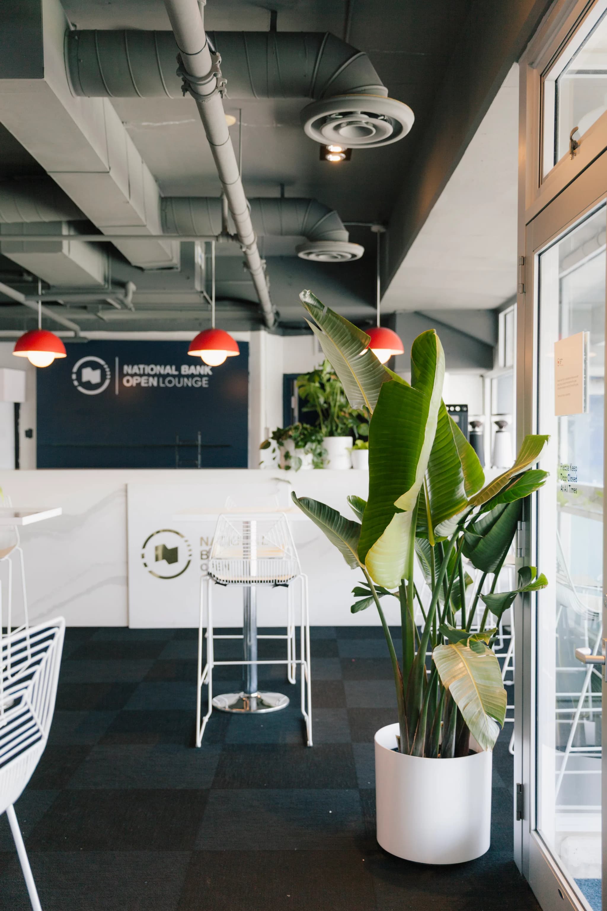 National Bank Open VIP lounge interior with Bird of Paradise plants, high tables, and tournament signage