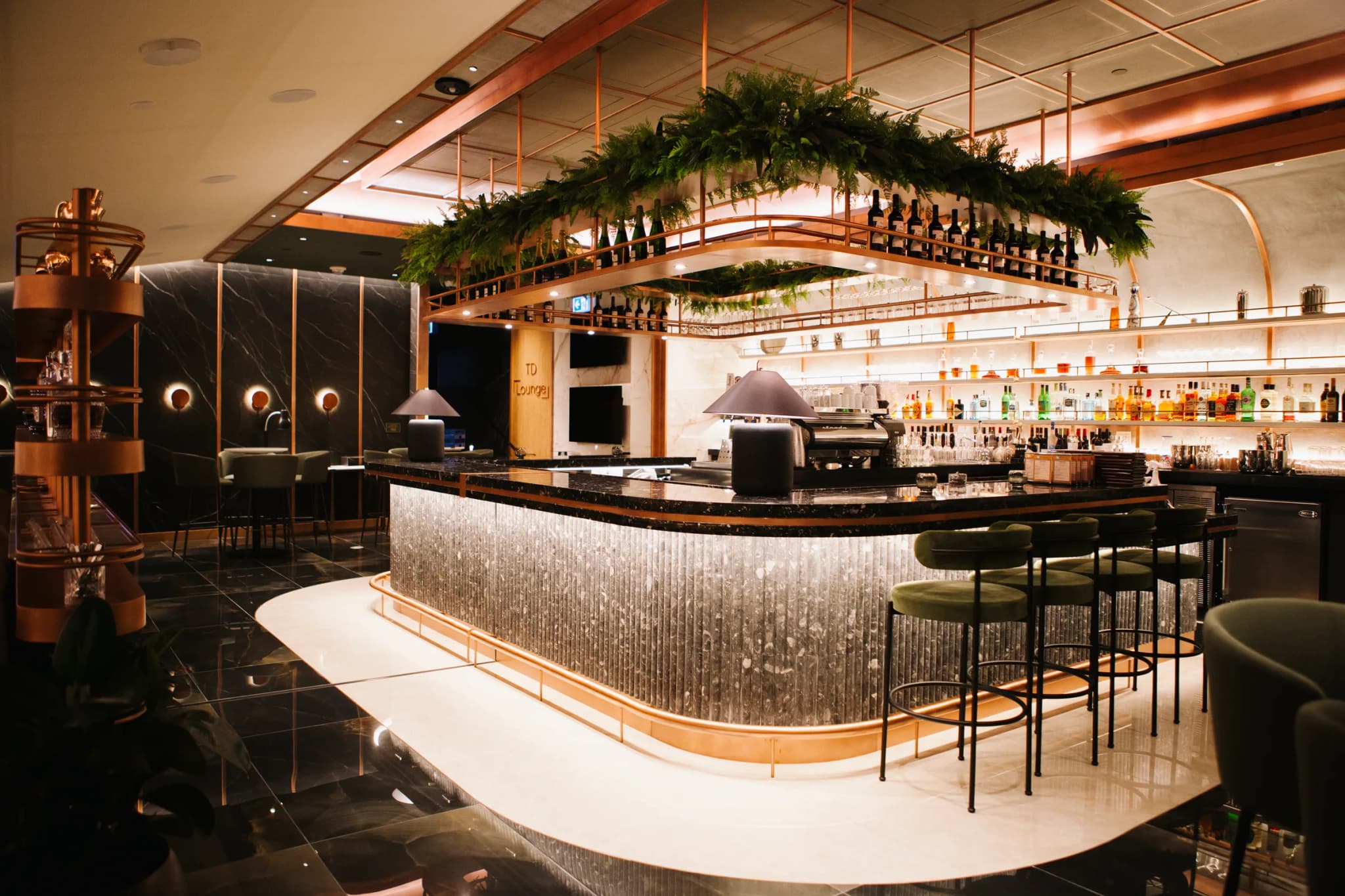 Curved bar with hanging fern and greenery installation above copper shelving at Rogers Centre VIP lounge