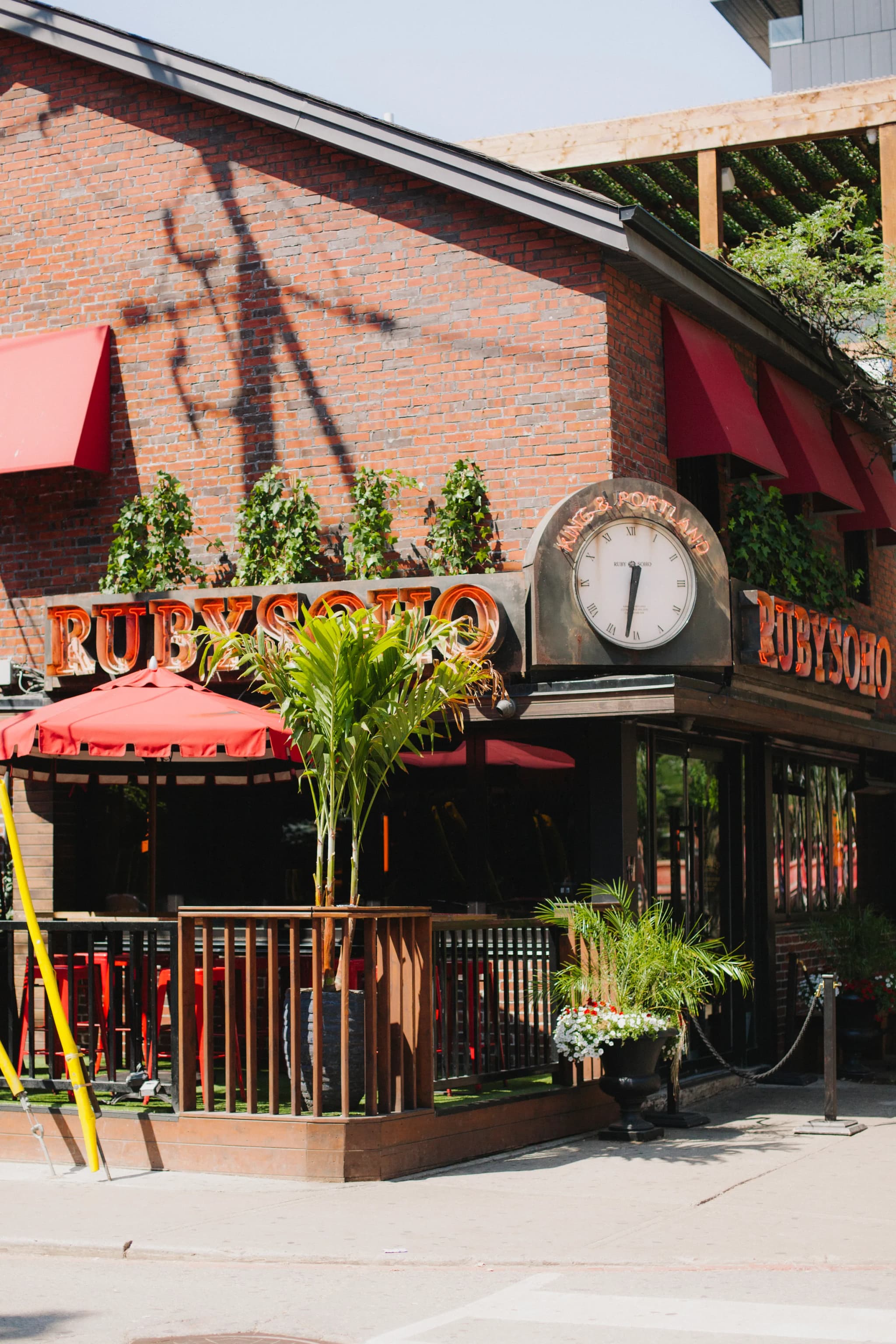 Ruby Soho restaurant facade with neon signage, clock and tropical palm plants on patio