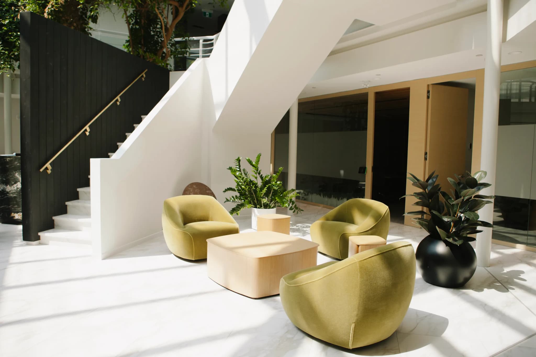 Double-height marble lobby with green velvet seating, ZZ plant, Rubber Plant and sculptural white staircase at Sentrex headquarters