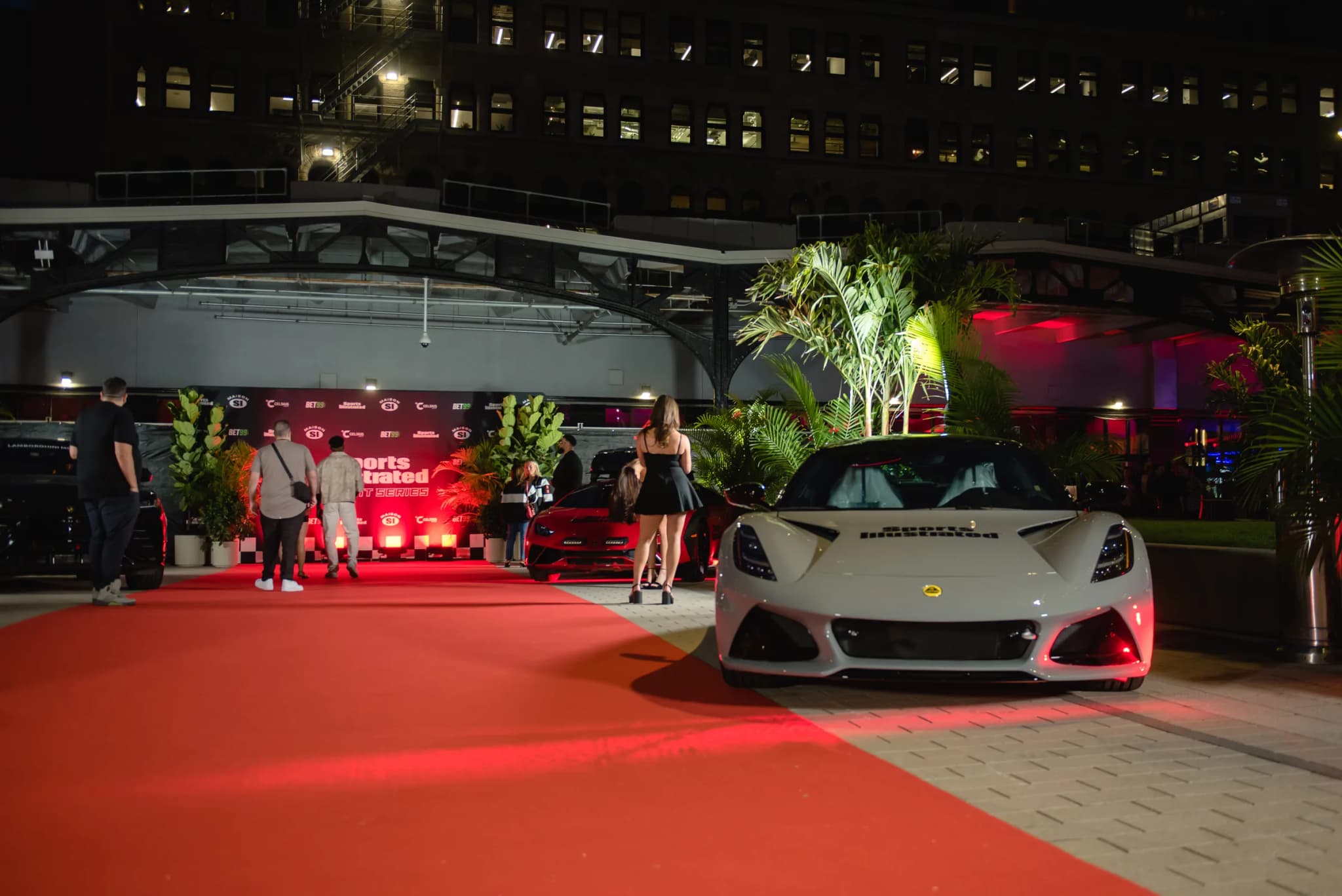 Sports Illustrated event entrance at night with red carpet, luxury cars, and tropical palm plants