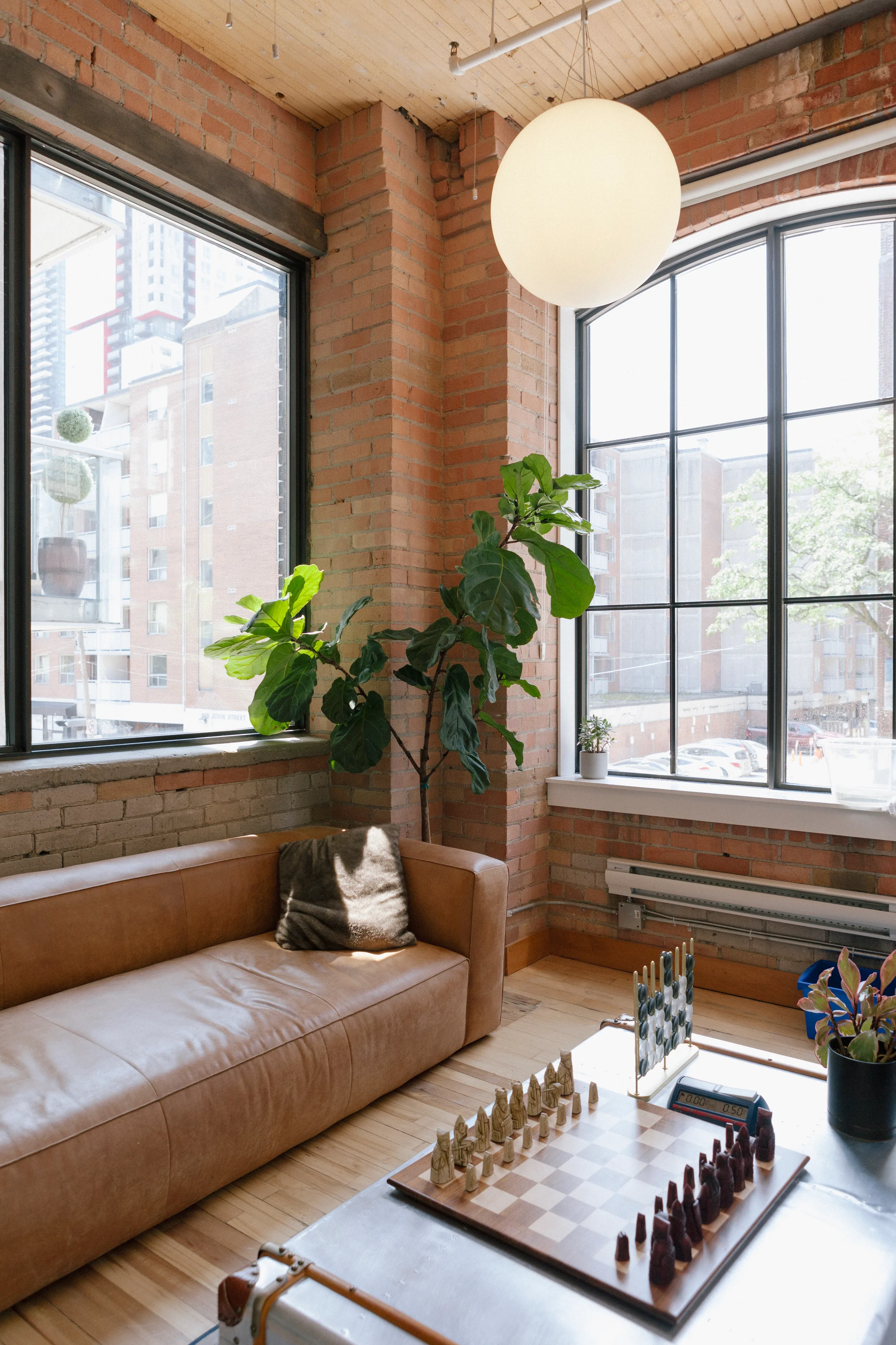 Bird of Paradise, Monstera and Schefflera in woven baskets by arched windows in brick loft