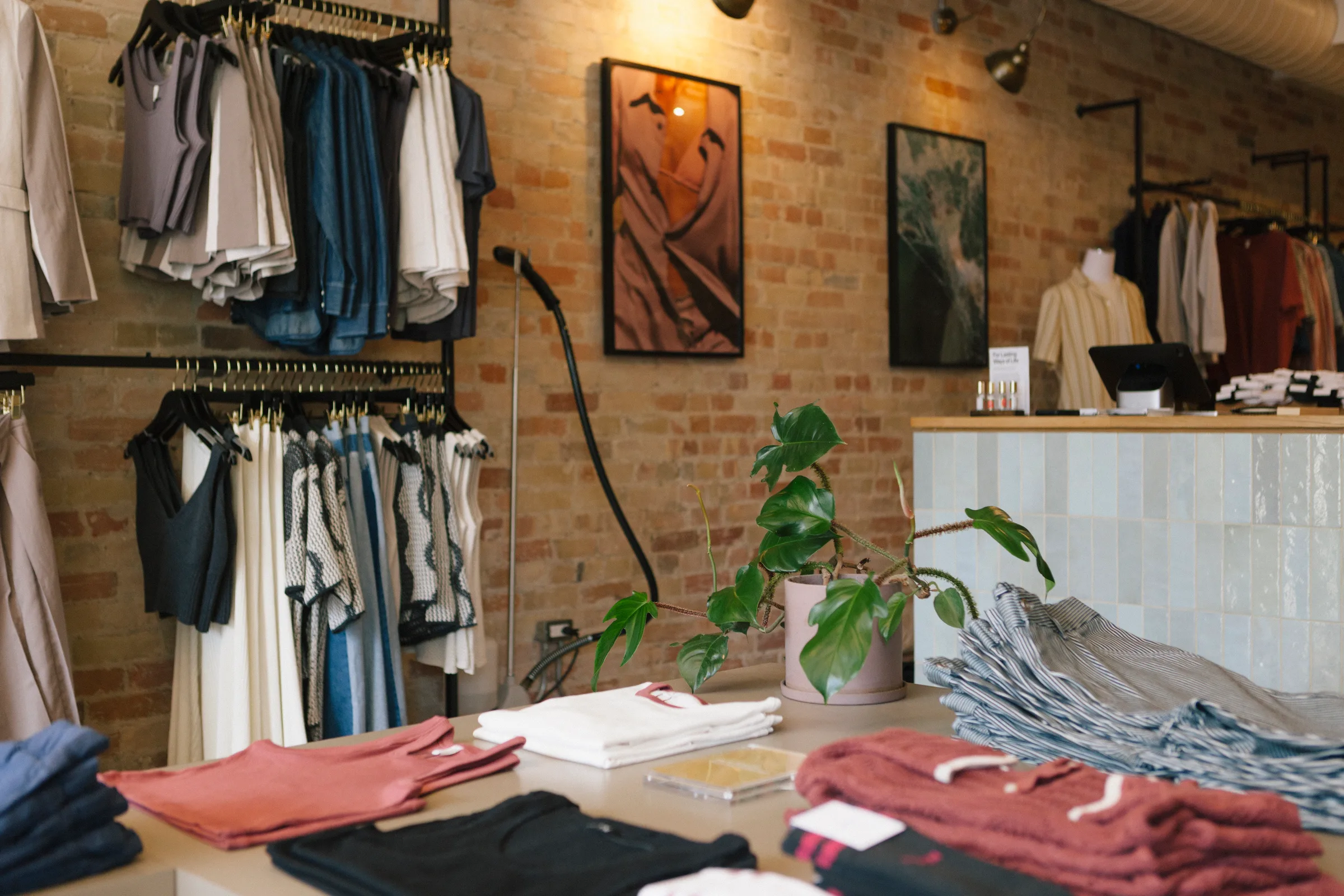 Monstera plant on counter with clothing displays and brick wall at KOTN
