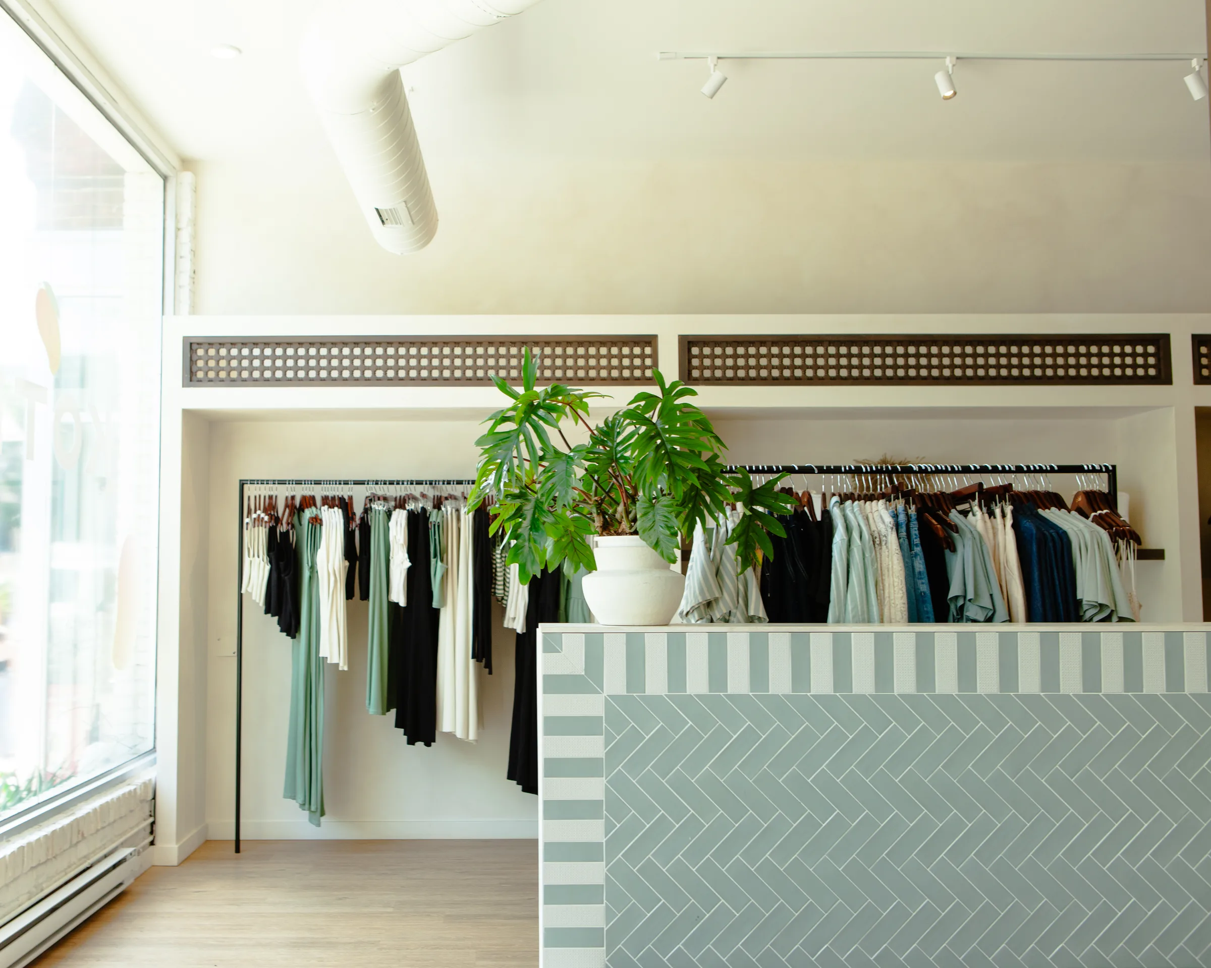 Herringbone tile counter with Monstera plant and clothing racks at KOTN Ossington