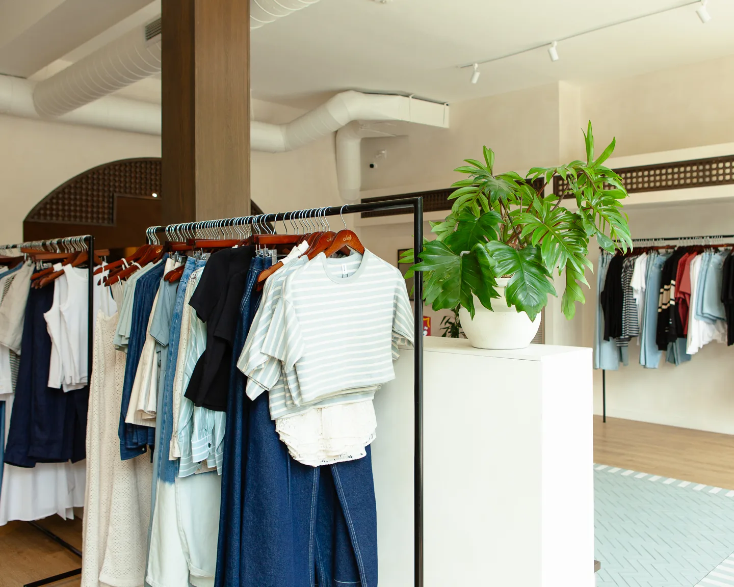 Monstera plant on white pedestal with clothing racks at KOTN Ossington